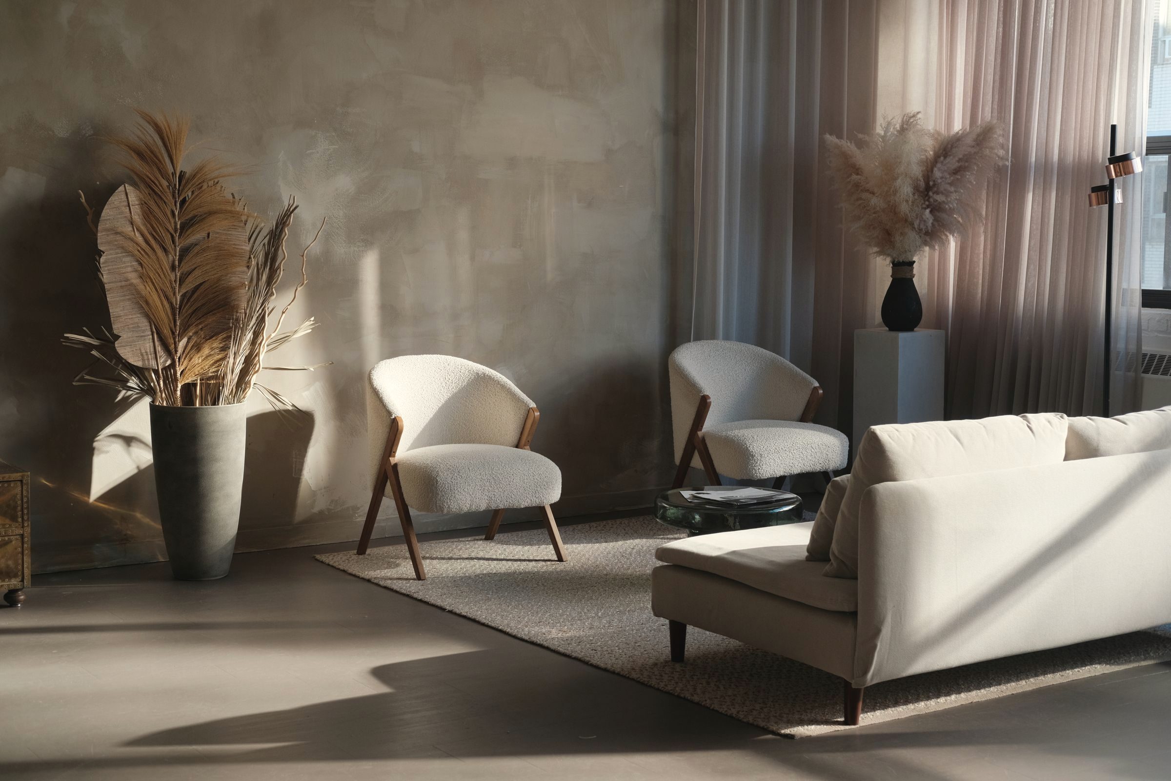Sitting room with a plaster wall, boucle armchairs, and low afternoon sun